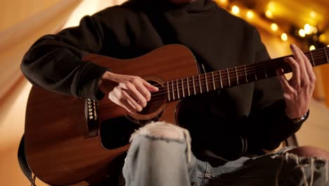 man plays the guitar and sings songs in a tent with light bulbs