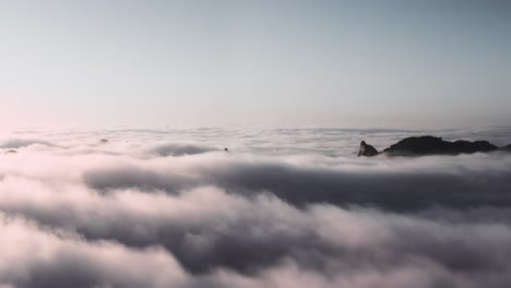 aerial: beautiful mountain peak rising above clouds at sunset, peaceful view