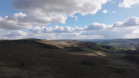 Aerial-drone-footage-flying-over-a-cloudy,-open,-dark-moorland-with-a-blue-sky