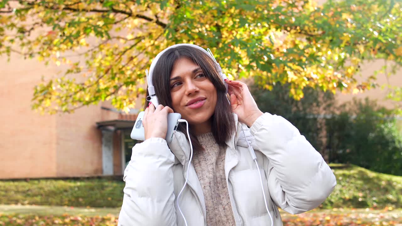 Woman enjoying music with headphones in a park during autumn