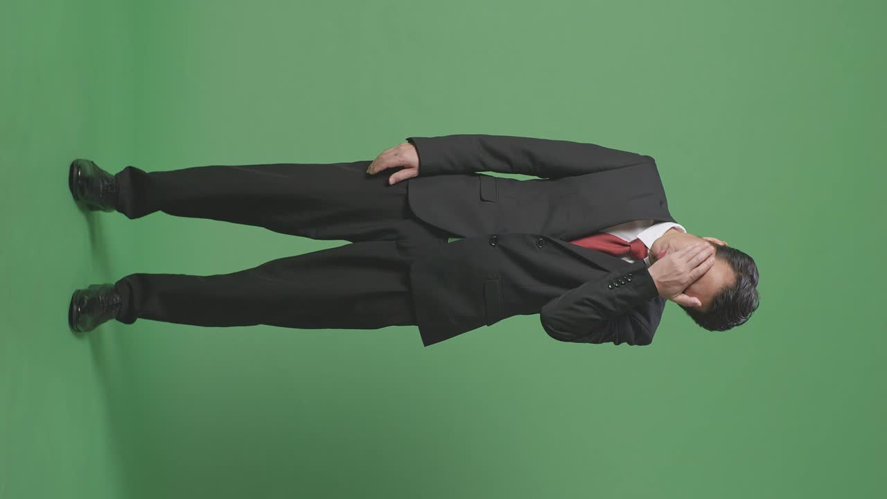 녹색 화면 앞에 서 있는 피곤한 아시아 사업가의 몸이 가득 차 있습니다.