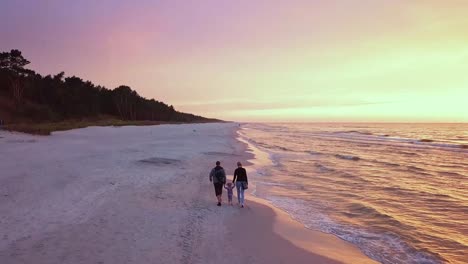 parents walking with a small child on a beach at sunset. happy family enjoying a walk on a beach. sunset beach walk drone footage.