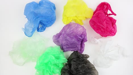 crumpled used plastic bags of different colors rotates on white background, top view, closeup, loop video, stopmotion animation, ecological problem