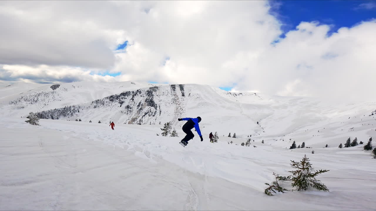 Snowboarder in black and blue outfit and helmet tries to jump up as rides by the slope. Practicing active life style and sport in the mountains.