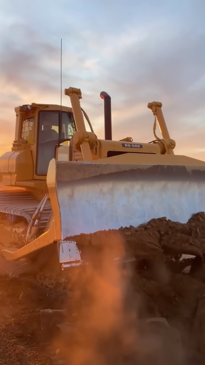 Video di un bulldozer al tramonto ripreso dal basso, che cattura il suo movimento potente e le tonalità dorate