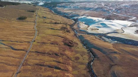 high angle forward drone shot over the vast grassy and snowy landscapes of the higlands in scotland during golden hour