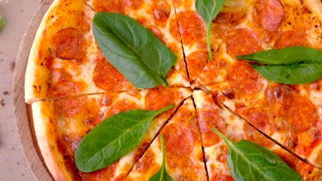 cortar pizza de salami con hojas de espinaca en una tabla de madera.