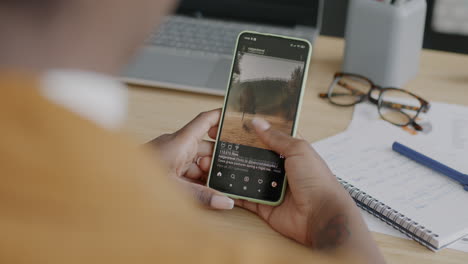 woman using smartphone at her desk, viewing photos/videos.