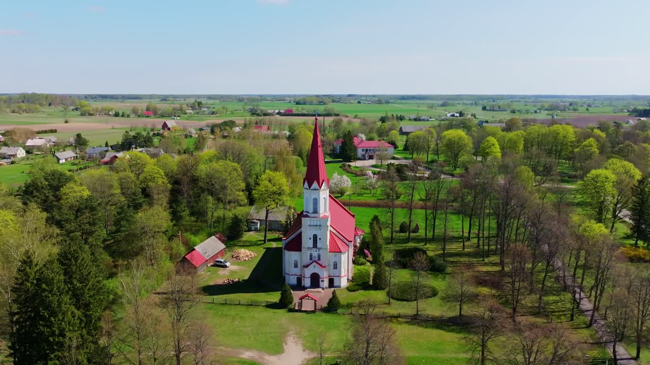 Calm spring morning view as drone circles iconic red-spired church in Rucava