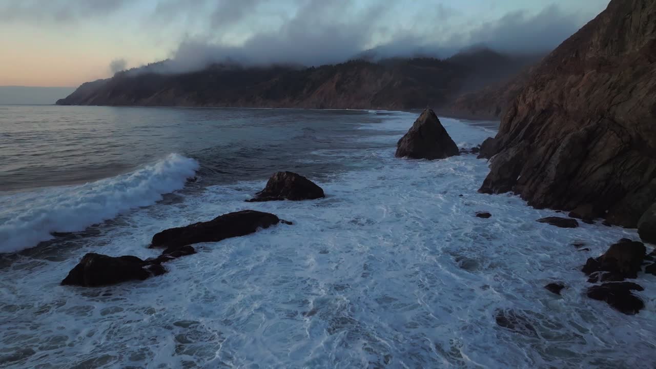 Northern California waves crashing bluffs cliffside mountain rocky rugged remote coastline aerial drone USAL Beach Campground sunset Sinkyone Wilderness surf swell black sand forward pan up motion