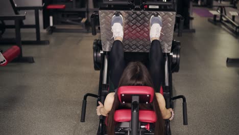 Backside-footage-of-a-sportive-brunette-girl-working-out-on-leg-press-at-the-gym.-Healthy-lifestyle,-fitness-and-recreation.