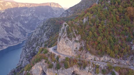 Car-driving-on-small-mountain-road-during-autumn-next-to-piva-lake-canyon-Montenegro,-aerial