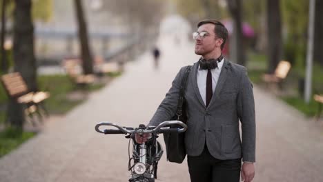 handsome young businessman goes with bicycle in park and smiles