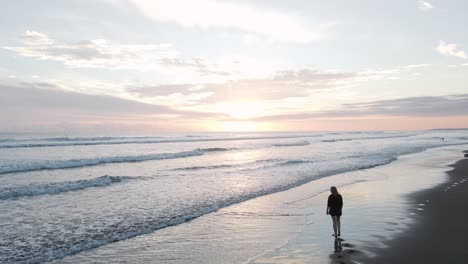 Aerial-slow-motion-of-the-Pacific-Ocean-surf-and-a-lady-walking-on-the-beach-under-a-beautiful-orange-sunset-at-Bandera-Beach-in-Costa-Rica