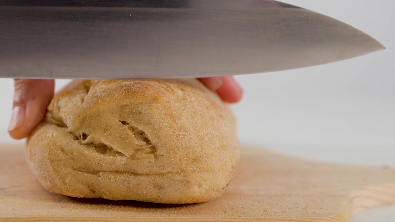 Close-up of hands slicing a fresh bun with a chef knife on a wooden board.