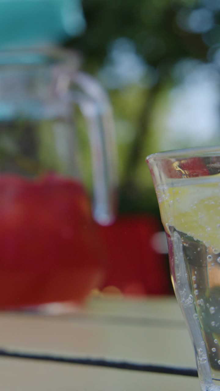 Una mano versa una bevanda rossa vivace in un bicchiere di acqua frizzante con limone