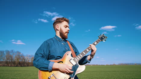 bearded guitarist playing among nature. musician playing the acoustic guitar on blue sky background. musical player with a guitar.