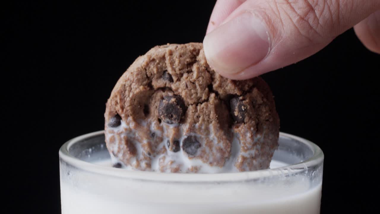 한 컵의 우유에 초콜릿  쿠키를 손으로 담그고 있습니다.