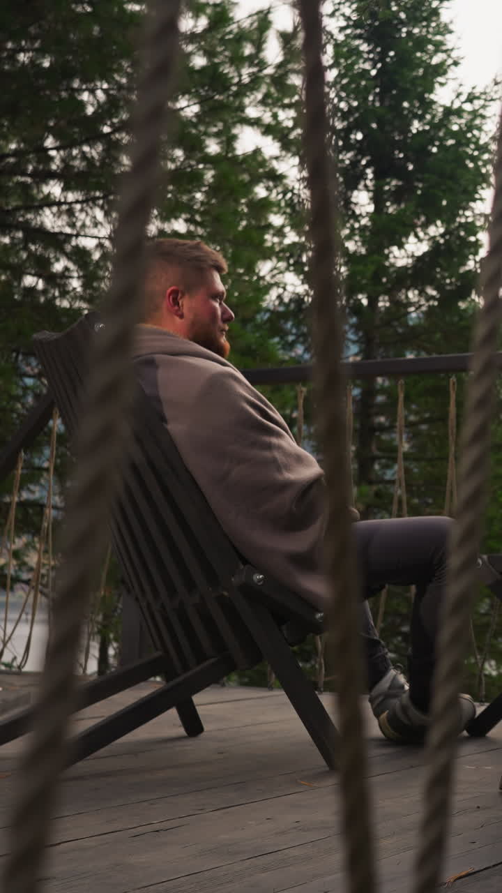 Young couple sits on terrace at eco-hotel. Woman and man enjoy accommodation with opportunity to observe fall nature. Wife sits with husband in armchairs at twilight