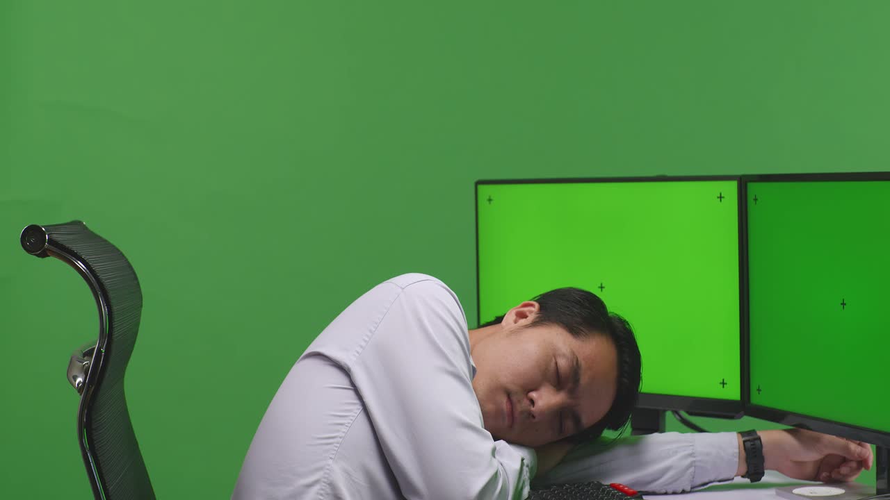 Close Up Of Tired Asian Man Sleeping While Working With Mock Up Multiple Computer Monitor In Green Screen Studio