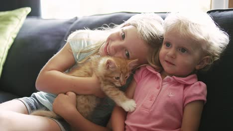 dos niñas sentadas en un sofá con un gatito y sonriendo