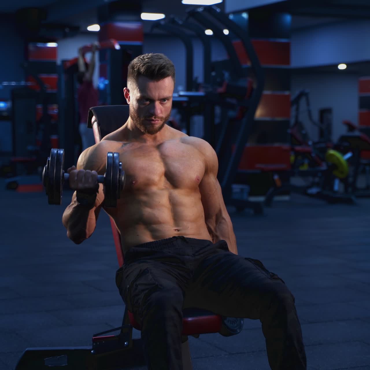 Bodybuilder che si allena nella palestra moderna. Lo sportivo è seduto su una sedia e allena i muscoli delle braccia con i manubri in un centro sportivo. Allenamento quotidiano