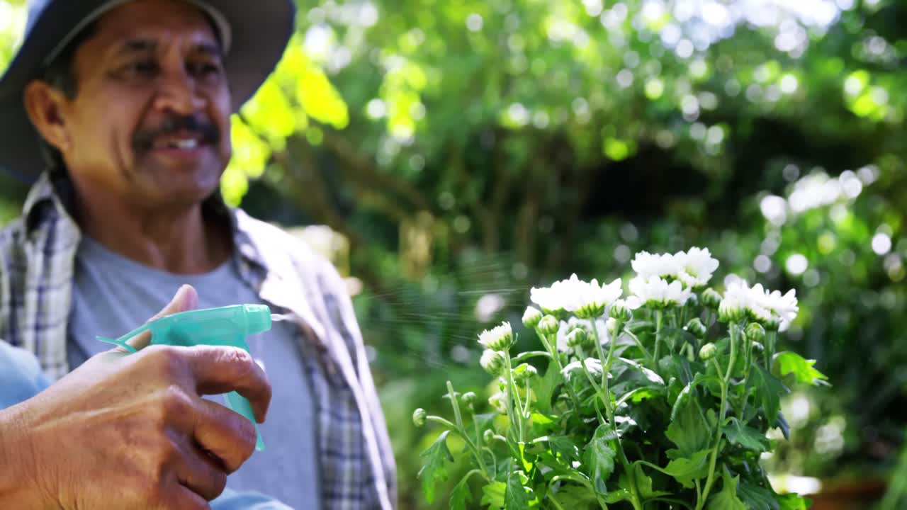 pareja de ancianos rociando agua en las flores