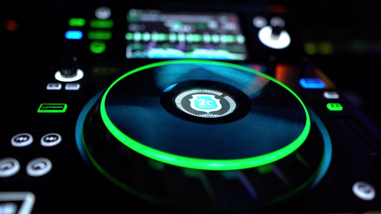 DJ controller with illuminated jog wheel during live club performance. Electronic music mixing setup with glowing interface and nightclub atmosphere