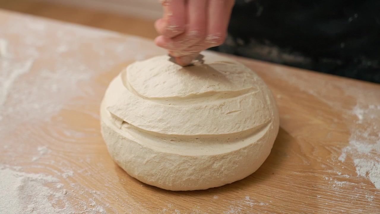 Close-up of Hand Scoring Raw Bread Dough on Wooden Table