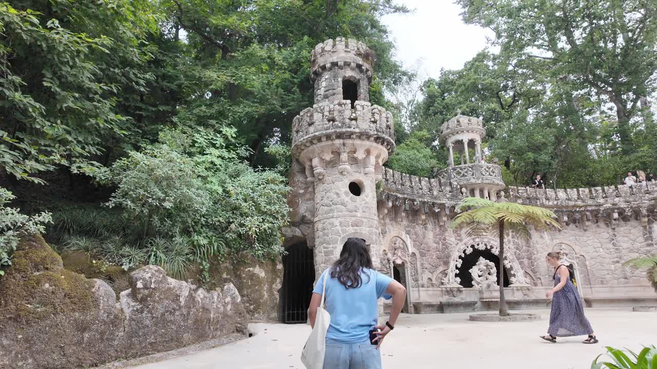 Woman exploring the lush gardens of Quinta da Regaleira in Sintra, Portugal, near ancient stone walls