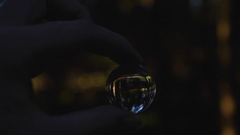 close up of a young female hand holding a small crystal ball reflecting landscape in an autumnal forest while spinning around