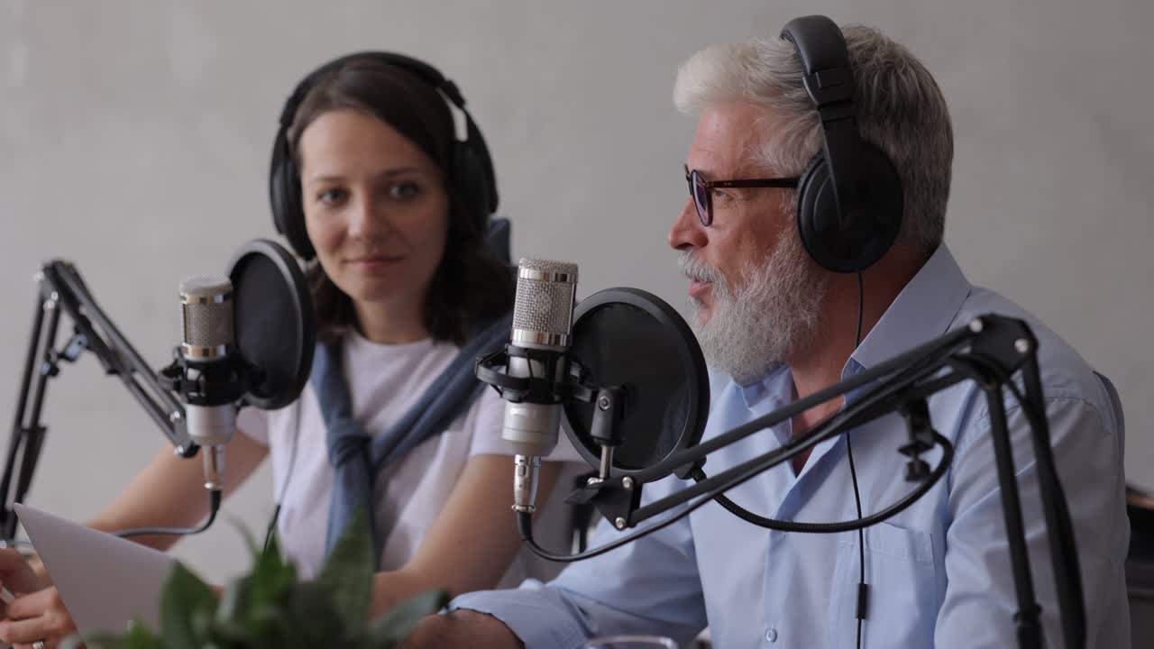 un hombre y una mujer graban un podcast o una entrevista con un micrófono en un estudio de grabación. un hombre adulto de cabello gris y una joven europea crean contenido de audio, graban anuncios y libros de audio