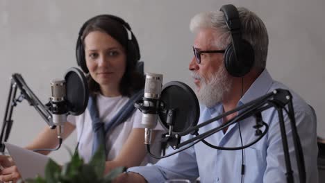 man and a woman record a podcast or interview with a microphone in a recording studio. an adult gray-haired man and a young european woman create audio content, record ads and audio books