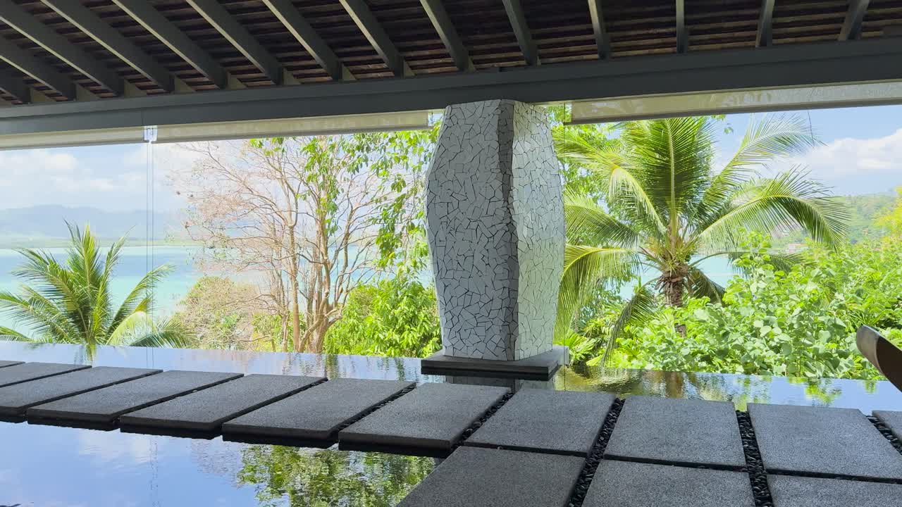 A tranquil view of a luxury resort pathway in Phuket, featuring lush greenery and a water feature under soft daylight