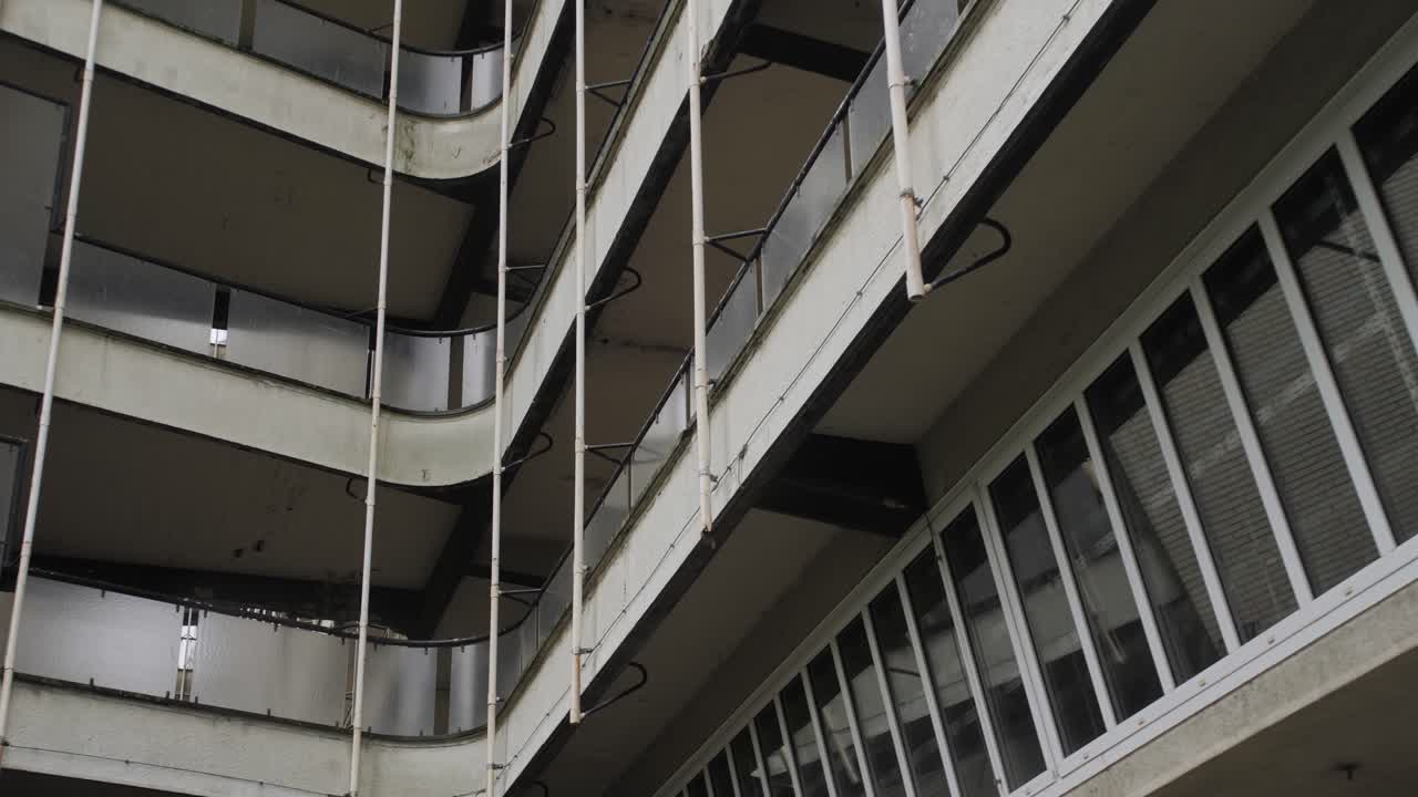 A detailed view of an aged apartment building with curved balconies featuring frosted glass railings and large vertical windows