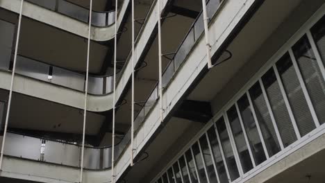 a detailed view of an aged apartment building with curved balconies featuring frosted glass railings and large vertical windows