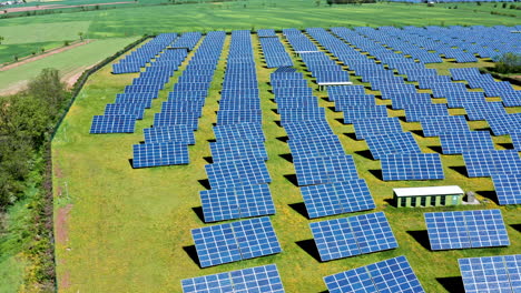 Rows-of-solar-panels-on-a-sunny-day-in-a-green-field,-aerial-view