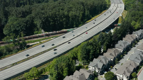 aerial drone view of a train passing under a busy highway in greater vancouver