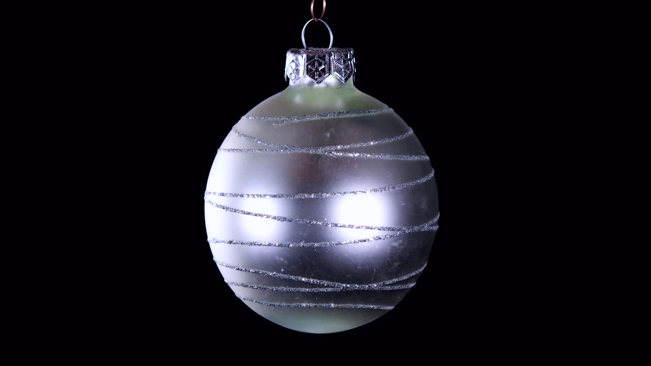 Einzelne silberne Weihnachtskugel mit Glitzerstreifen und schwarzem Hintergrund, Nahaufnahme.