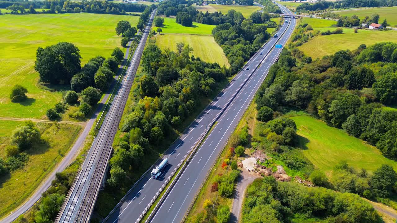 Aerial view of parallel railway line and highway running through rural farmland and forest landscape