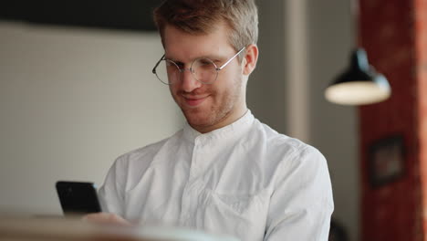 relaxed-man-is-surfing-internet-by-modern-smartphone-and-smiling-sitting-alone-in-cafe-or-coworking-space