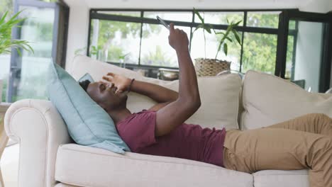 video of happy african american man lying on sofa and having video call on smartphone