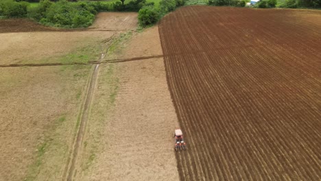 Una-Filmación-Aérea-Siguiendo-A-Un-Tractor-Naranja-Labrando-Una-Tierra-De-Cultivo-Que-También-Revela-Una-Línea-De-árboles,-Algunas-Aves,-Muak-Klek,-Tailandia