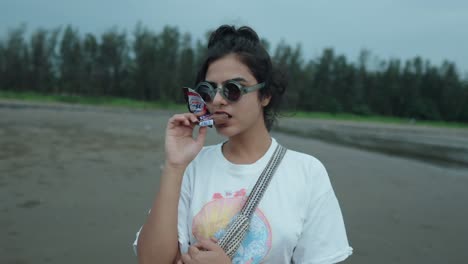 A-carefree-young-Asian-woman-in-sunglasses-offering-a-bite-of-the-chocolate-bar-to-the-camera