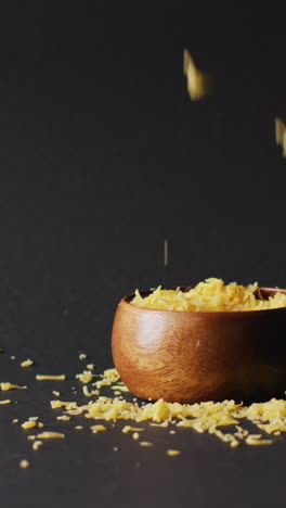 video de queso rallado cayendo en y alrededor de un cuenco de madera, contra un fondo gris con espacio de copia