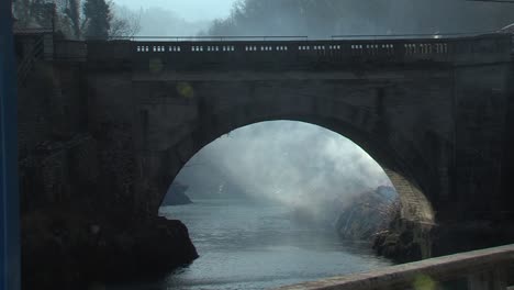 smoke rolling below bridge after huge field fire, river flowing below, contrast