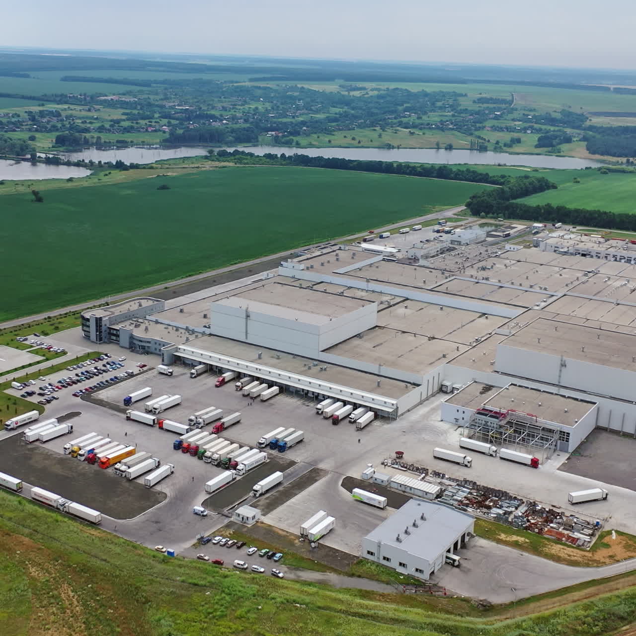 Aerial view of a modern industrial territory in the countryside. Huge manufacturing structure with several car parking outdoors.