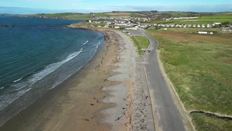 drone footage of coastal road with distant village. sandy beach and calm atlantic, west cork ireland