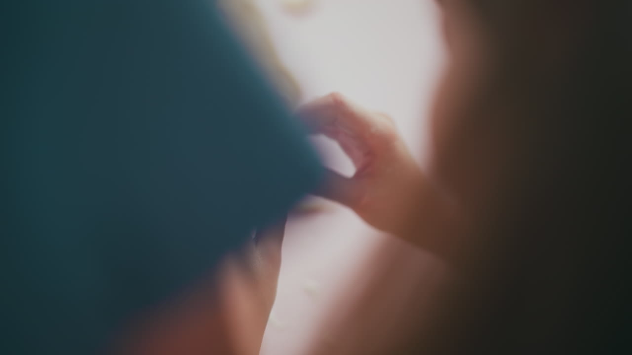 Back view of young child holding and pressing pancake dough pieces together with floury fingers on pink table during playful baking activity, pink cutter cone visible in background