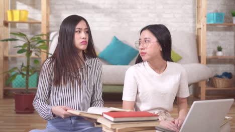 two tired asian students with textbooks and a laptop are sitting on the floor in the living room